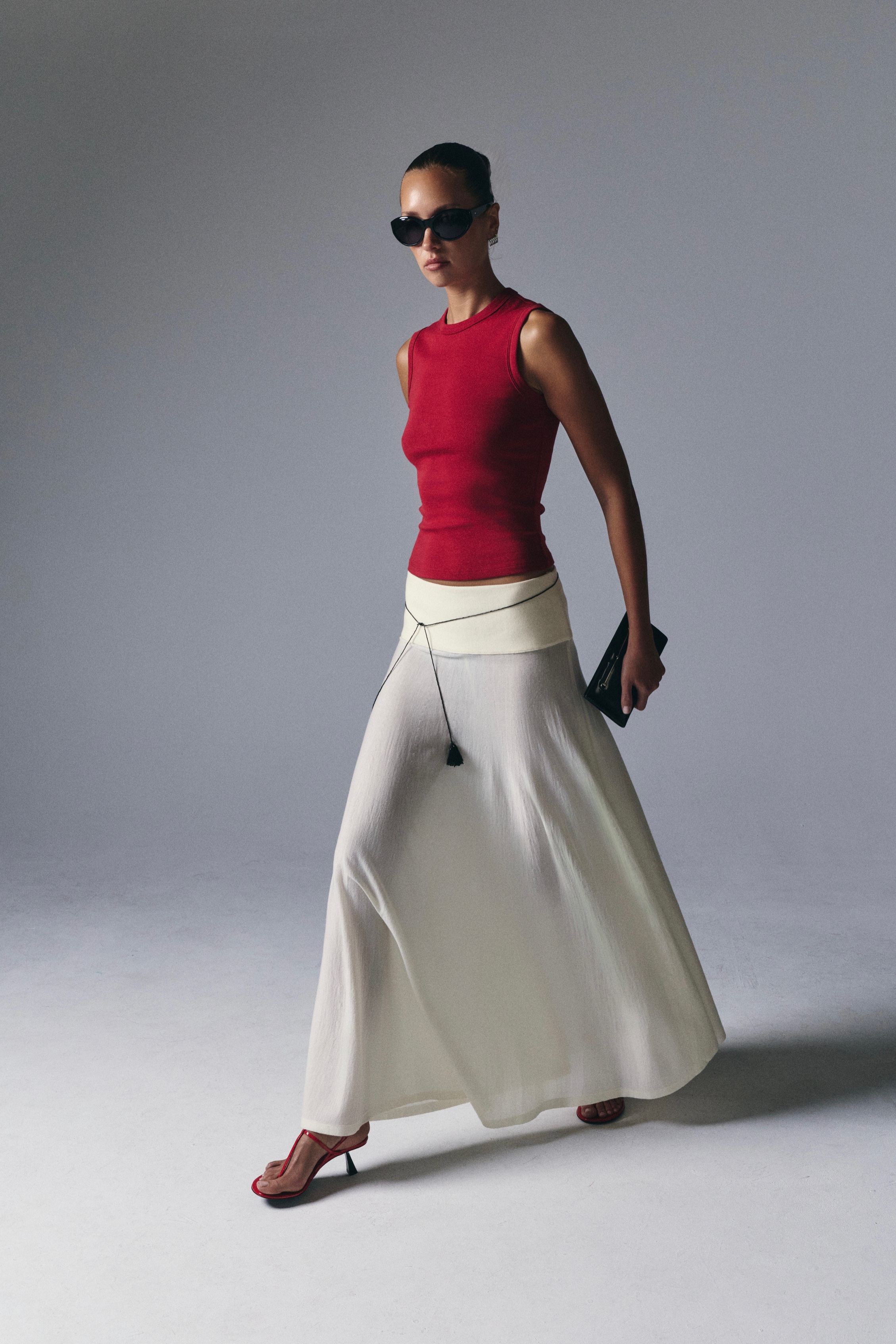 Model in a red tank and ivory skirt mid-stride against a grey studio backdrop